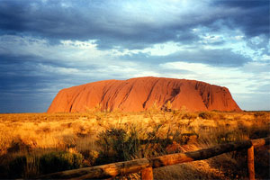 Uluru sits majestic and coloured bold red under a bright blue sky